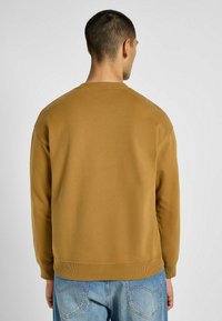 Felpa in cotone marrone con maniche lunghe, colletto e vita a costine, caratterizzata da una texture liscia e una vestibilità comoda.