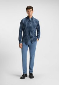 Karierte Hemd in Blau und Marine mit langen Ärmeln, kombiniert mit hellblauen Hosen und schwarzen Schuhen. Glatte Stoffqualität, lässige Passform.