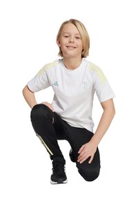 Witte korte mouwen shirt met gele schouderstrepen en het Juventus-logo, gecombineerd met zwarte broeken met gele accenten en zwarte sportschoenen.