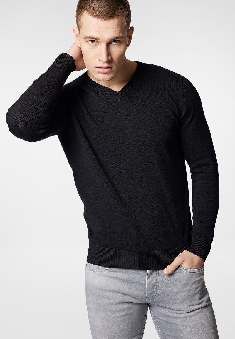 Czarny sweter z dekoltem w serek i długimi rękawami, z prążkowanymi mankietami i dołem, zestawiony z jasnoszarymi spodniami. Charakteryzuje się miękką teksturą dzianiny.