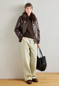 Brun faux læder bomberjakke med pelskrave, brun sweater, lyseblå videbukser, brune sko og en sort tote taske.