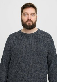 Tamsiai mėlynas megztinis su tekstūruotu raštu, apvaliu kaklu ir raglano rankovėmis. Charakterizuoja minkštas, storas audinys.