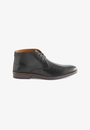 Stivale chukka in pelle nera con punta arrotondata, dotato di un design con lacci, fodera in pelle marrone e suola marrone a contrasto con striature sottili.