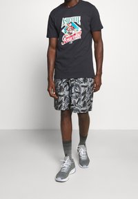 Černé tričko s grafikou "Asheville Tourists", doplněné o šedé vzorované kraťasy, šedé tenisky a pruhované ponožky.