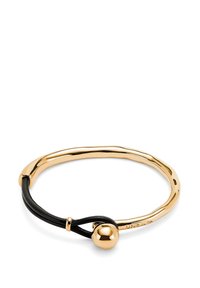 Pulsera de metal en tono dorado con un diseño suave y curvado, que presenta un cordón de cuero negro y un detalle de cierre esférico.