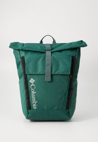 Sac à dos vert à rabat fabriqué en tissu durable, avec une sangle supérieure, une poche avant, des zips latéraux et une finition texturée. Arbore le logo Columbia.