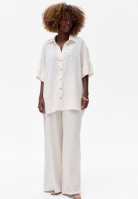 Lichtgewicht linnen shirt in off-white met een knoopsluiting en korte mouwen, gecombineerd met wijde broekspijpen met subtiele borduursels.