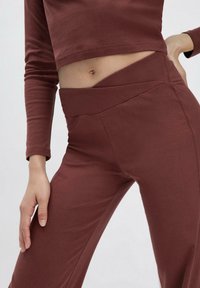 Bordeaux crop top en bijpassende high-waisted broek gemaakt van zachte, rekbare stof; heeft een gladde textuur en een schuin waistband.