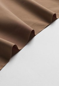 Bruine stoffen gordijnen met een zachte, gladde textuur en zachte golven. De rand heeft een subtiele krul, tegen een lichte achtergrond.