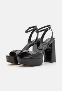 Sandales à plateforme en cuir verni noir avec une pointe ouverte, des brides de cheville ajustables et des talons épais et hauts avec une finition brillante.