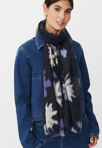 Czarny szal w kwiatowe wzory w odcieniach bieli i fioletu, o miękkiej teksturze i frędzlach na brzegach, noszony na jeansowej kurtce.