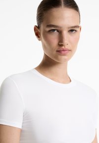 T-shirt bianco a maniche corte con scollo rotondo, realizzata in tessuto liscio. Presenta una forma aderente con cuciture minime e un design semplice.