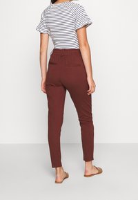 Housut viininpunaisella värillä, joissa on joustava vyötärö, takataskut ja sileä kangas. Yhdistetty raidalliseen lyhythihaiseen paitoihin.