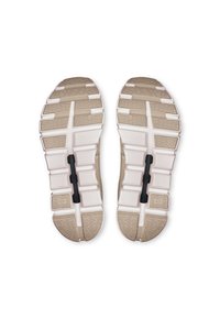 Semelles de chaussures avec une surface texturée beige et des éléments de rembourrage blancs ; elles présentent plusieurs rainures et une pièce centrale en caoutchouc noir.