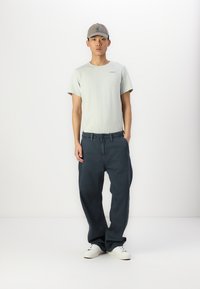 Lys grå t-skjorte, avslappet passform, kombinert med marineblå løse jeans. Hvite joggesko og en grå caps fullfører det uformelle antrekket.