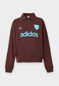 Rjav pulover s polo ovratnikom, ki ima svetlo modro "adidas" logo in podrobnosti ščita, izdelan iz mehkega materiala s sproščenim krojem.