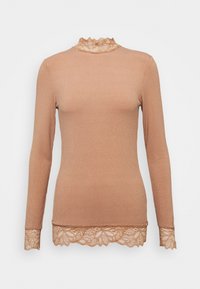 Långärmad topp i ljusbrun ribbad tyg med hög spetskrage och spetsdetaljer vid ärmsluten och nederkant, vilket skapar en texturerad detalj.