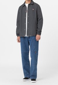 Grå jacka med tryckknappar, elastiska ärmslut och sidofickor, som är ihop med blå vida denimjeans med ett lappar. Svarta slip-on skor.