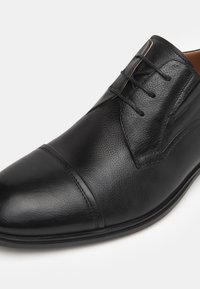 Schwarzer Lederschuh mit strukturiertem Finish, Schnürdesign und abgerundeter Spitze. Verfügt über eine kontrastierende Naht entlang der Vorderseite und eine glatte Sohle.