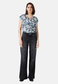 Bloemmotief top in teal, wit en roze; gecombineerd met high-waisted, wijdvallende zwarte jeans. Soepele stof en casual pasvorm.