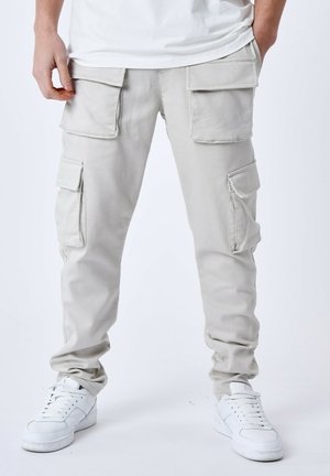Pantalones cargo de color gris claro con múltiples bolsillos grandes, corte ajustado, hechos de una tela duradera, combinados con zapatillas blancas.