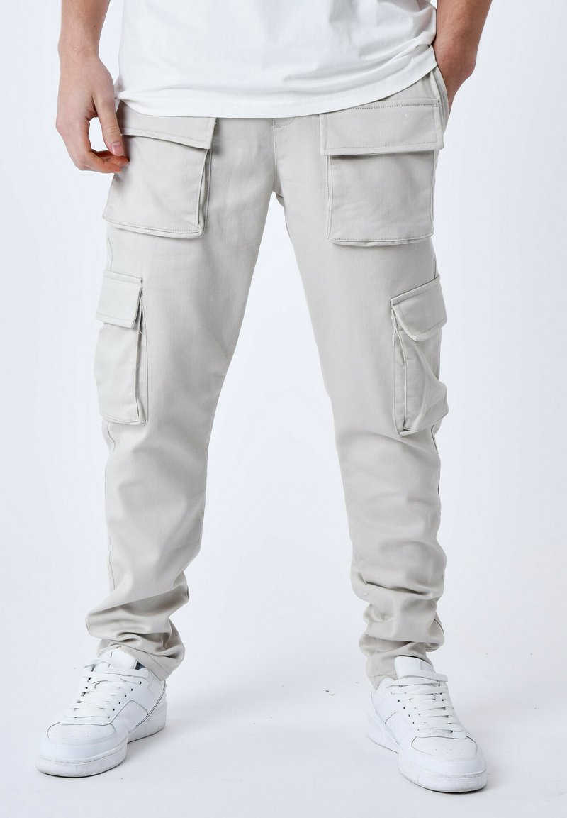 Pantaloni cargo grigi chiari con diverse tasche grandi, vestibilità affusolata, realizzati in tessuto resistente, abbinati a sneaker bianche.