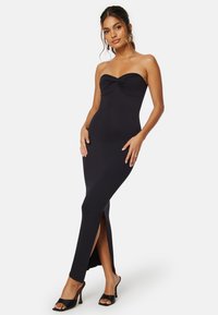 Svart ribbad maxiklänning med strapless-design, samlad byst och sidoklyftor. Modellen bär svarta klacksandaler.