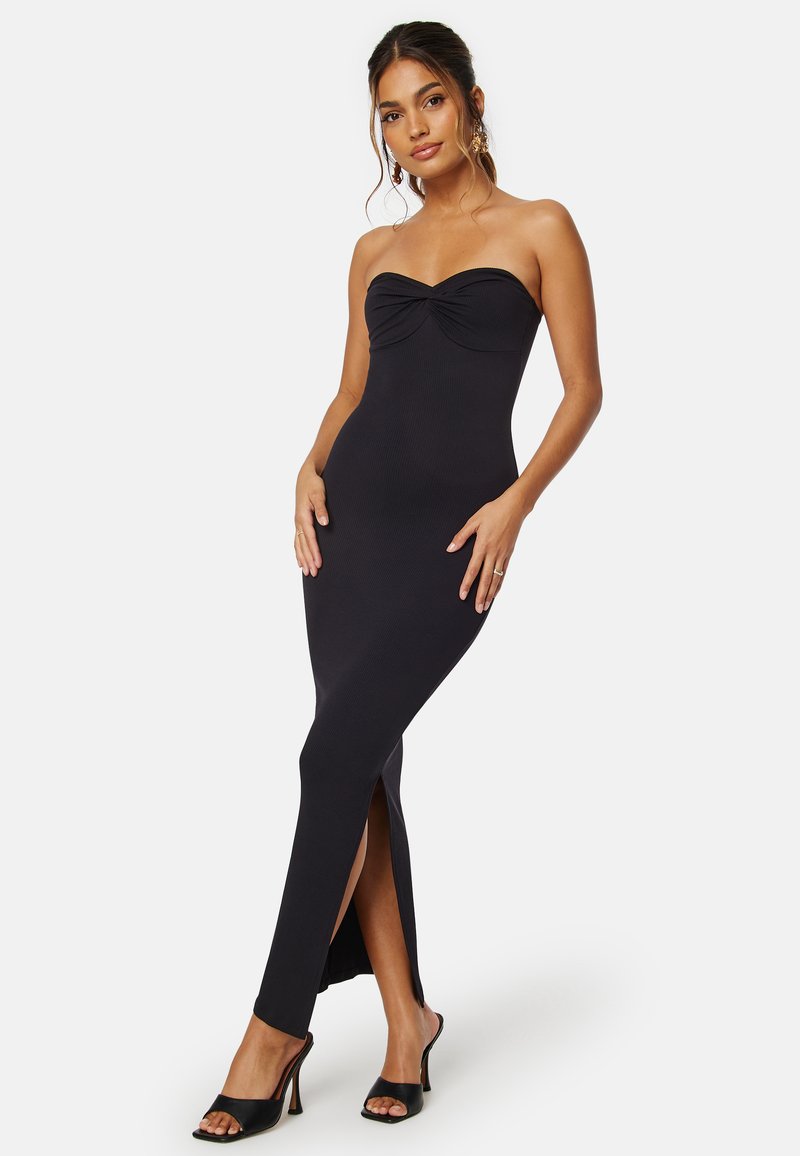 Svart ribbad maxiklänning med strapless-design, samlad byst och sidoklyftor. Modellen bär svarta klacksandaler.