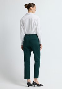 Witte long sleeve shirt met een kraag, gecombineerd met op maat gemaakte groene broek en zwarte hoge hakken. Eenvoudig ontwerp met minimale accenten.