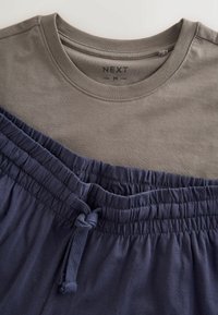 Maglietta marrone a girocollo taglia media abbinata a pantaloncini blu navy con elastico in vita e coulisse annodata.