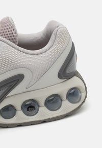 Scarpa sportiva grigia chiara con tomaia in rete testurizzata, dettagli in sintetico liscio e una distintiva ammortizzazione a bolle nella suola.
