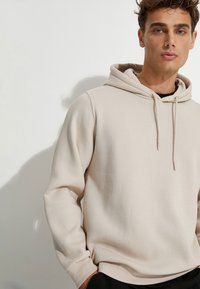 Sudadera beige clara hecha de una suave tela texturizada. Presenta una capucha con cordón y puños acanalados, con un corte holgado.