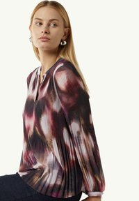 Faltige Bluse mit langen Ärmeln im mehrfarbigen Muster, das Nuancen von Lila, Pink und Creme zeigt, mit einem Keyhole-Ausschnitt.