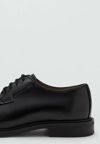 Czarny skórzany but o gładkim wykończeniu, zaokrąglonym nosku i niskim, warstwowym obcasie. Posiada wiązanie na sześć dziurek.