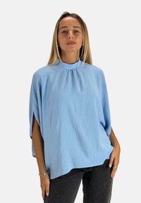 Top azzurro chiaro a maniche corte con scollatura alta e dettagli plissettati. Realizzato in un tessuto testurizzato con una vestibilità ampia e fluida.