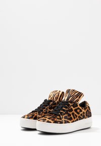 Sneaker con stampa leopardata, con tomaia testurizzata, lacci neri e una suola bianca spessa, dotate di un collare imbottito per un comfort aggiuntivo.