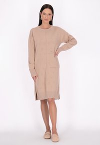 Abito in maglia beige con maniche lunghe, colletto rotondo e spacco laterale. Presenta una tasca frontale e un motivo floreale testurizzato. Vestibilità casual.