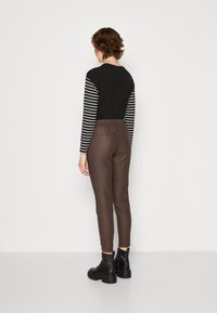 Un haut noir à manches longues avec des rayures blanches, associé à un pantalon extensible marron et des bottines noires. Design minimaliste avec une taille élastique et des poches.