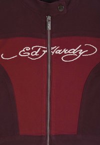 Bordowa i ciemnoczerwona kurtka z zamkiem z przodu oraz białym haftowanym napisem "Ed Hardy" na klatce piersiowej.
