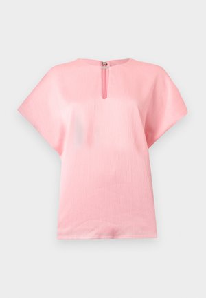 Blouse courte à manches courtes de couleur rose tendre avec un tissu texturé et un petit col en forme de goutte d'eau fixé par une fermeture argentée.