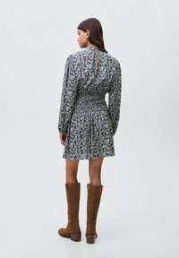 Šaty s kvetinovým vzorom, s smockovaným pásom, dlhými rukávmi a prestrihom na chrbte. Nosené s hnedými nubukovými čižmami po kolená.