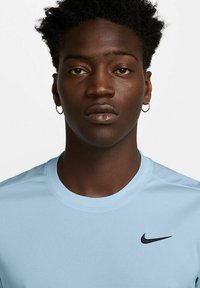 Šviesiai mėlynas Nike sportinis marškinėlis su apvalia iškirpte ir juodu logotipu kairėje pusėje. Sklandus paviršius, trumpomis rankovėmis ir laisvu siluetu.