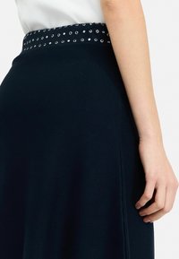 Gonna blu navy con un corpo testurizzato e una vita con occhielli in metallo argentato. Il tessuto presenta un motivo a righe per un dettaglio aggiuntivo.