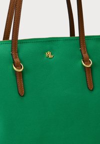 Grønn lerrets tote bag med brune lærreimer og gullfarget hardware. Har et preget "RLL"-logo på forsiden.