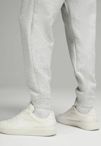 Lichtgrijze sweatpants met geribbelde boorden, in combinatie met witte sneakers met een gladde textuur en subtiele branding aan de zijkant.