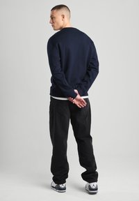 Navy blue crewneck sweatshirt, cotton blend, relaxed fit, paired with black pants. Features ribbed cuffs and a minimalist design.