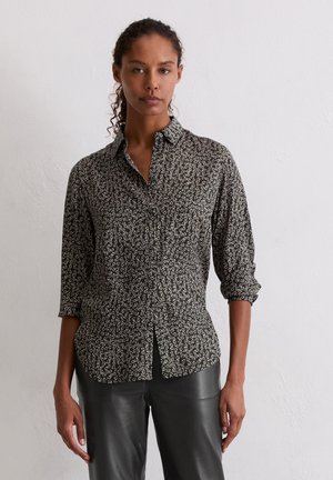 Schwarzes, blumiges Hemd mit Knopfleiste, kragenlosem Ausschnitt, hochgerollten Ärmeln und lässigem Schnitt. Mit kleinen weißen Blumenmustern überzogen.