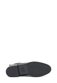 Suela de zapato de cuero negro con una superficie lisa, tacón rectangular y logo aplicado. Presenta un agarre texturizado para tracción.