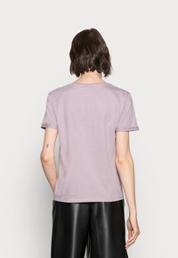 Camiseta de manga corta lila, hecha de algodón suave, con un escote redondo y puños de manga enrollados, mostrada desde la parte trasera.