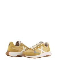 Zapatillas de ante amarillas con un diseño en forma de X blanca, acentos de malla, cordones redondos y una suela de goma marrón claro.